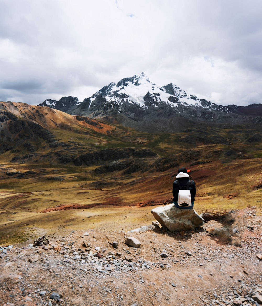 person sitting on rock in front of moutain