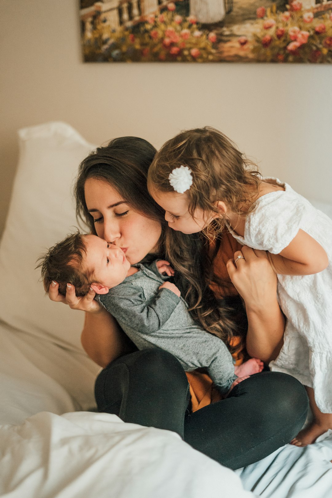 Mother kissing baby boy with young daughter on bed