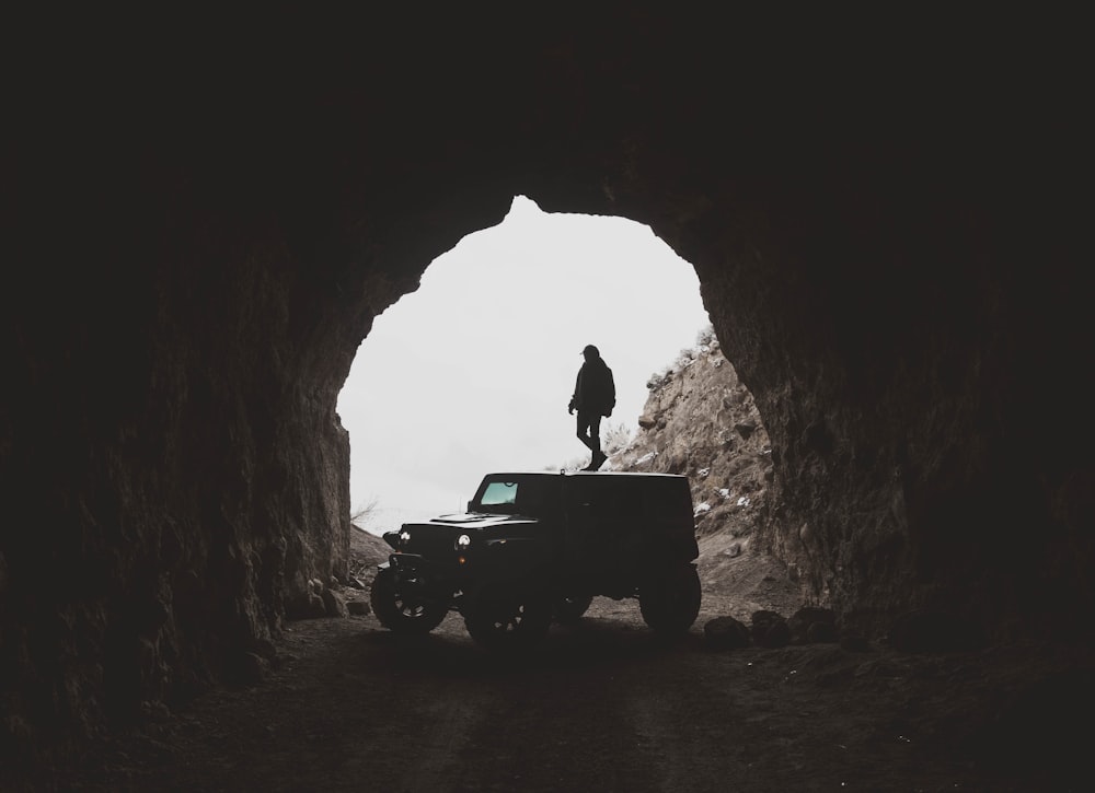 person standing on black sports utility vehicle inside cave