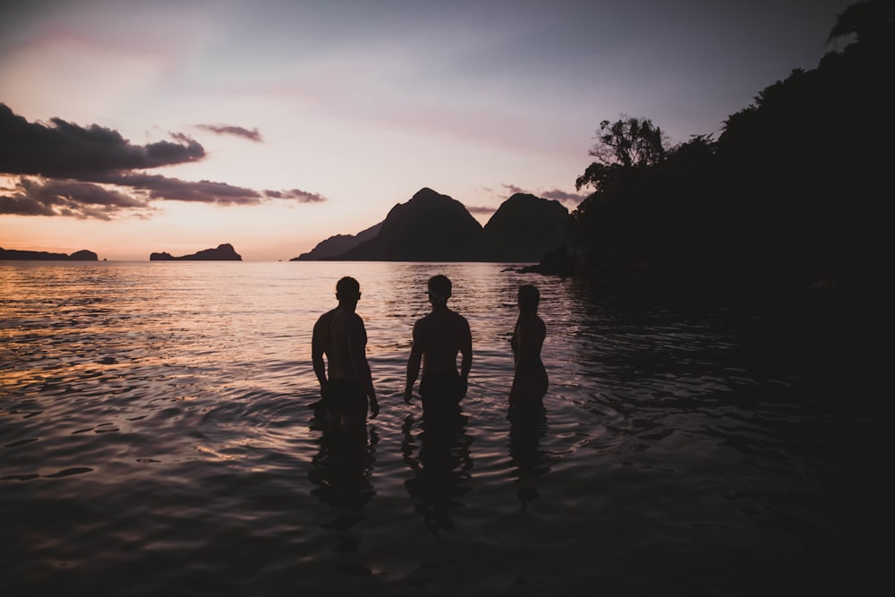 silhouette of three person standing on calm body of water