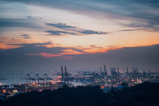 A serene seaport at sunrise with cargo ships and cranes silhouetted against the glowing sky, symbolizing sustainable logistics.