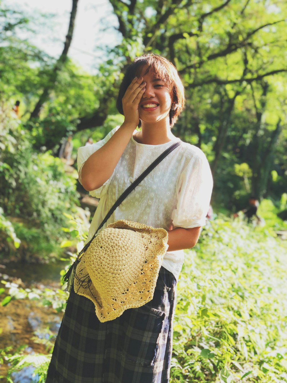 woman standing while smiling cover her right eye with her right hand