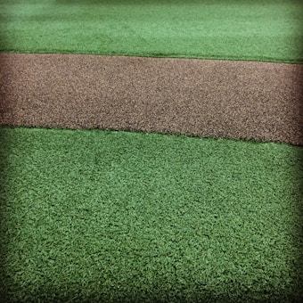 A textured surface featuring a path-like strip of coarse brown gravel running horizontally through two areas of vibrant green artificial grass.