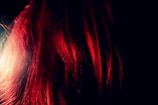 A close-up of vibrant red hair strands illuminated against a dark background, creating a striking contrast with the dark surroundings.