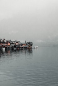 A serene lakeside village with quaint boats docked and mountains in the background during golden hour.