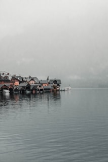 A serene lakeside village with quaint boats docked and mountains in the background during golden hour.