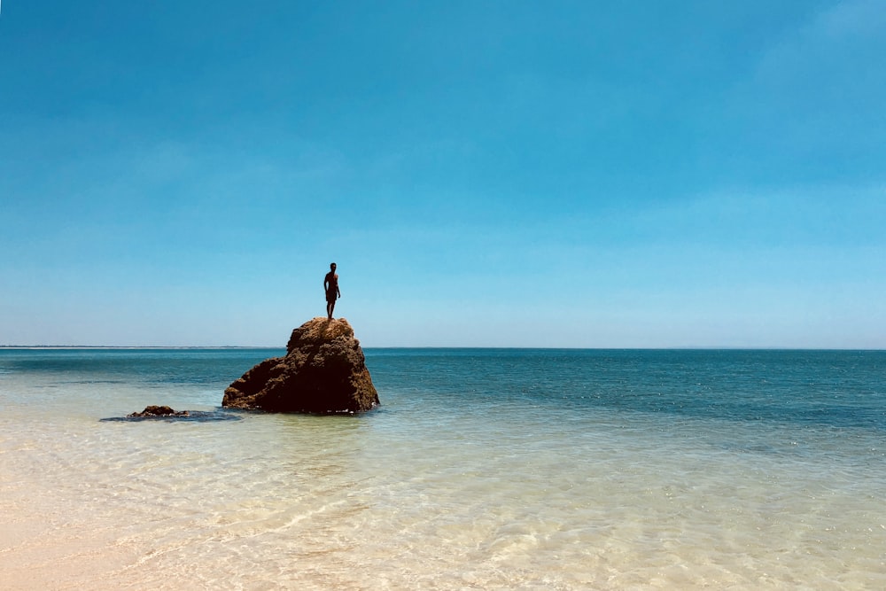 Persona de pie en la cima de la roca a través del mar durante el día