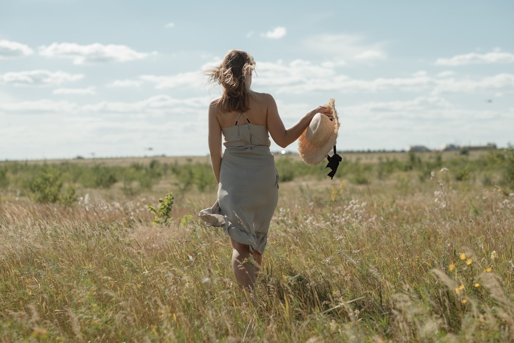 woman wearing grey midi dress holding straw hat during daytime