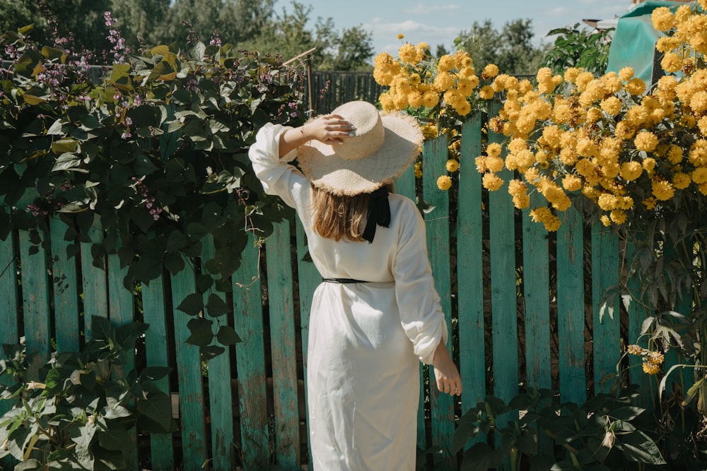 woman facing wooden fence with crawling vine and flowers