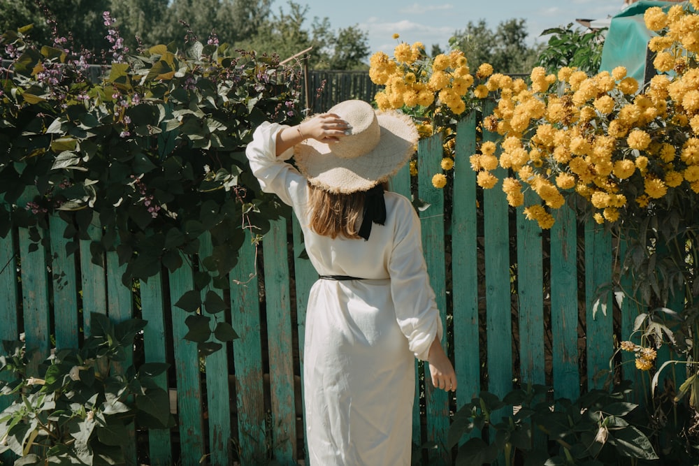 mulher de frente para a cerca de madeira com trepadeira rastejante e flores