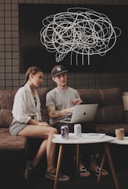 young man and lady sitting on sofa using MacBook