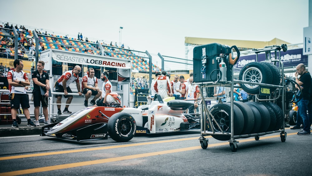 white and red Formula 1 car at pit stop with crew during daytime