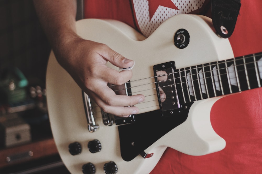 persona tocando la guitarra blanca y eléctrica