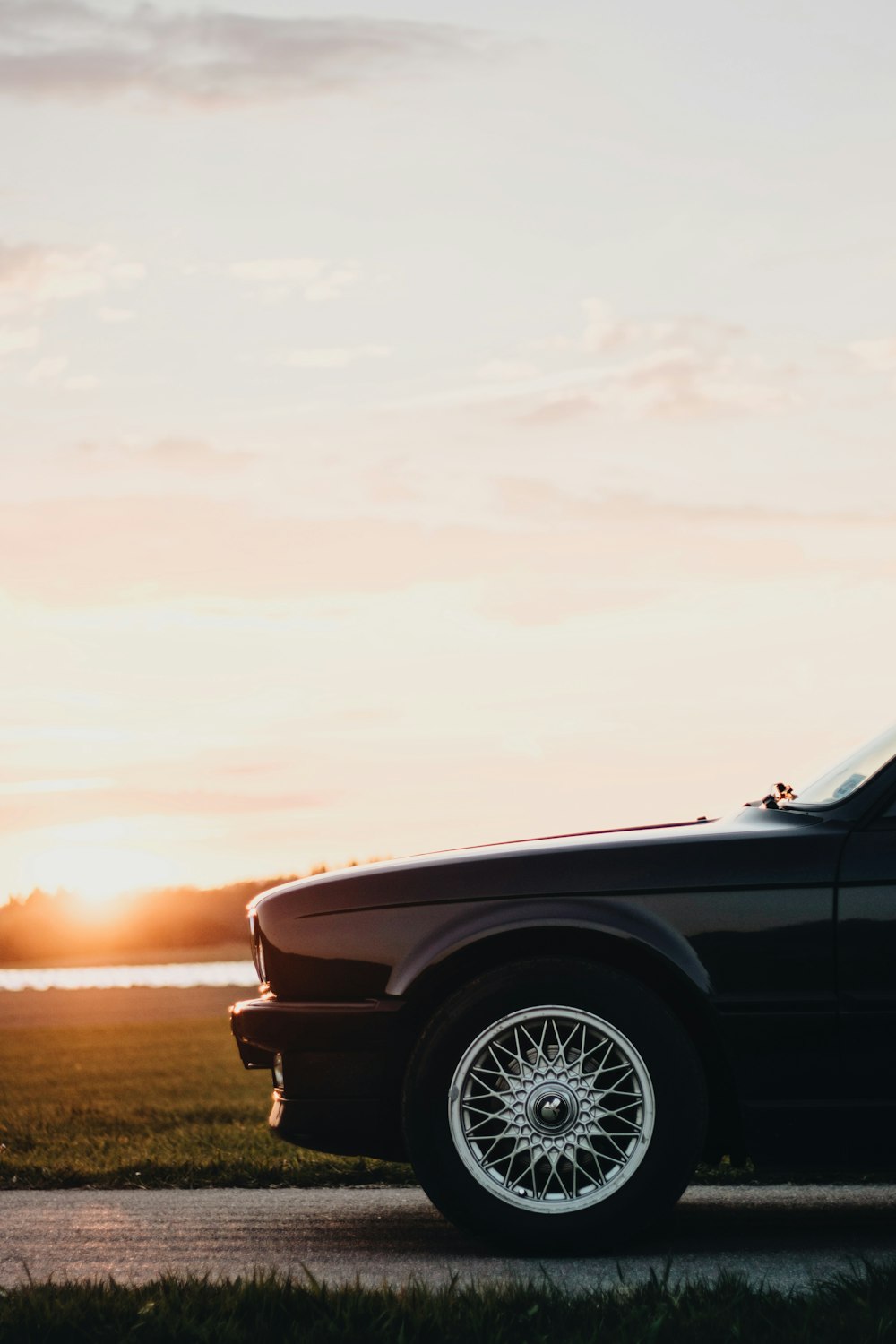 black muscle car parked on pavement near grass during sunrise