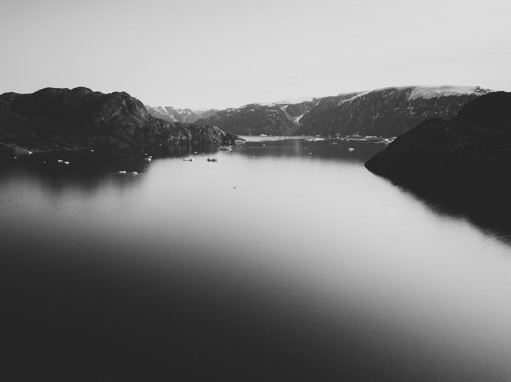 fotografia aérea de lago cercado com colinas em fotografia em escala de cinza