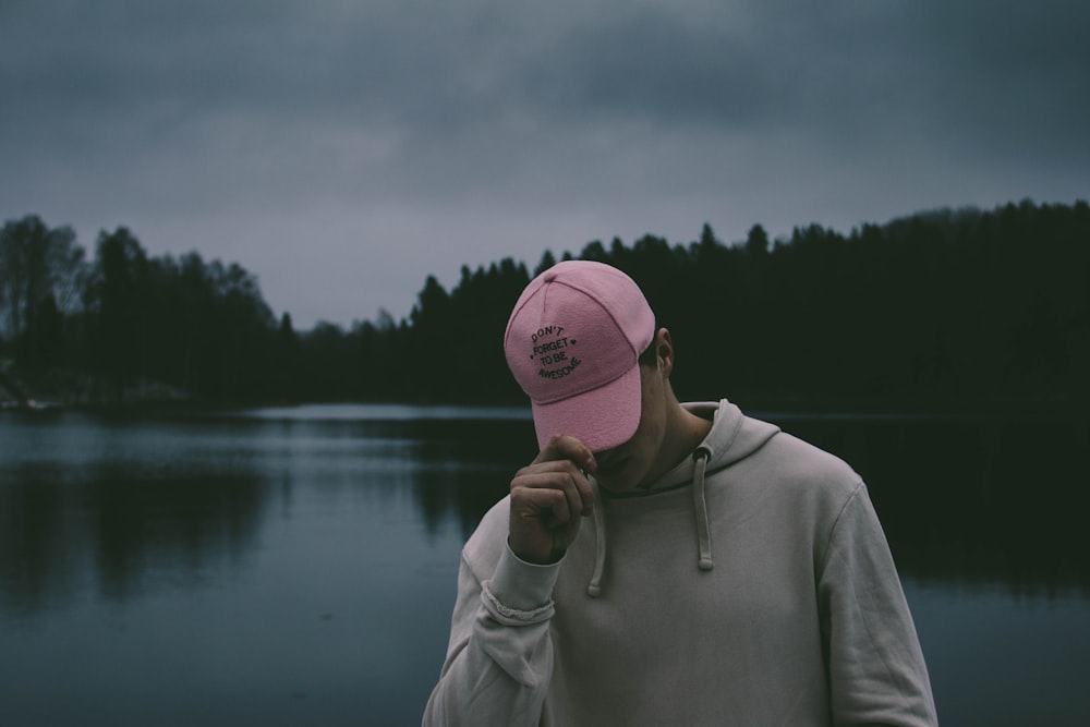 Foto Hombre vestido con una sudadera con capucha blanca sosteniendo su gorra  rosa con vista al cuerpo de agua – Imagen Gris gratis en Unsplash