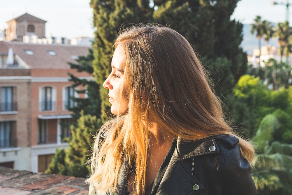 woman in black leather jacket near tree and house