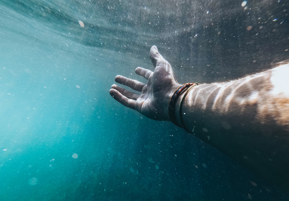 Person, die rechte Hand mit Armbändern im Gewässer zeigt
