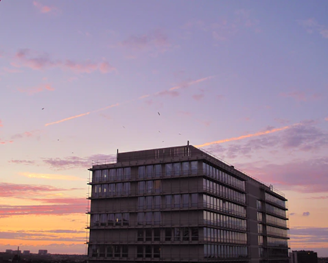 A sleek, modern office building with a global cityscape in the background during sunset.