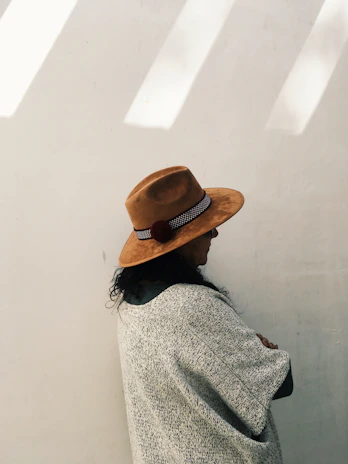 A woman wearing a maroon embroidered poncho, standing against a beige wall with warm sunlight.