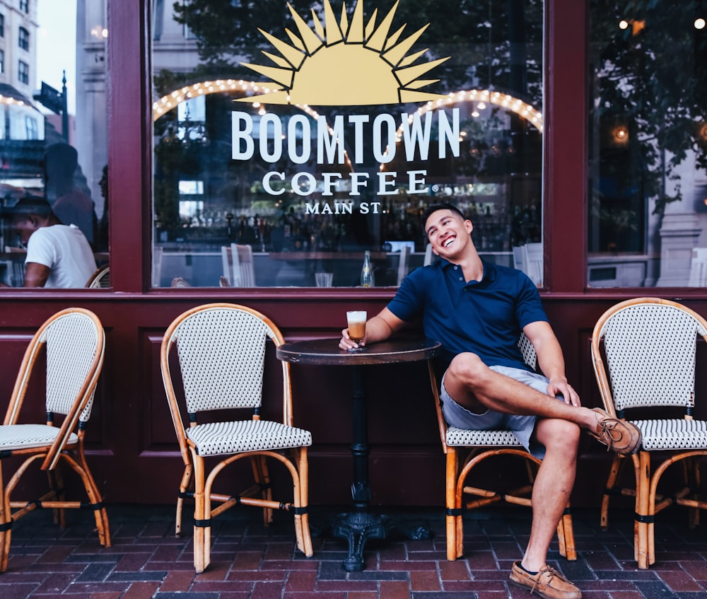 man sitting on wicker chair beside table outside Boomtown Coffee bar at daytime