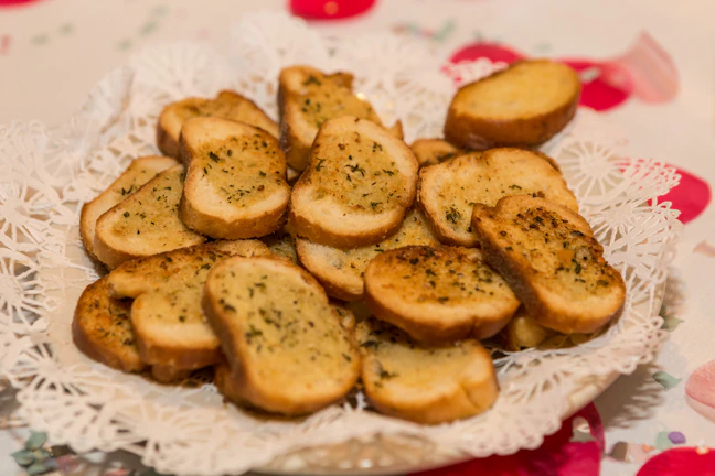 A close-up of a delicate cream-colored plate with gold-rimmed edges holding a slice of artisan bread topped with sage green floral spread and edible petals.