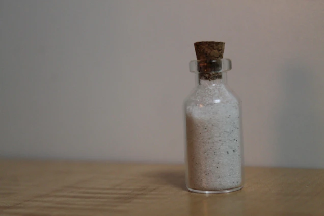 Close-up of a glass jar filled with authentic Ibiza sand, resting on a white surface with soft blue Mediterranean light.