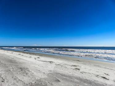 A serene beach scene with gentle waves and a jar of Lasibicencas body scrub resting on smooth white sand.