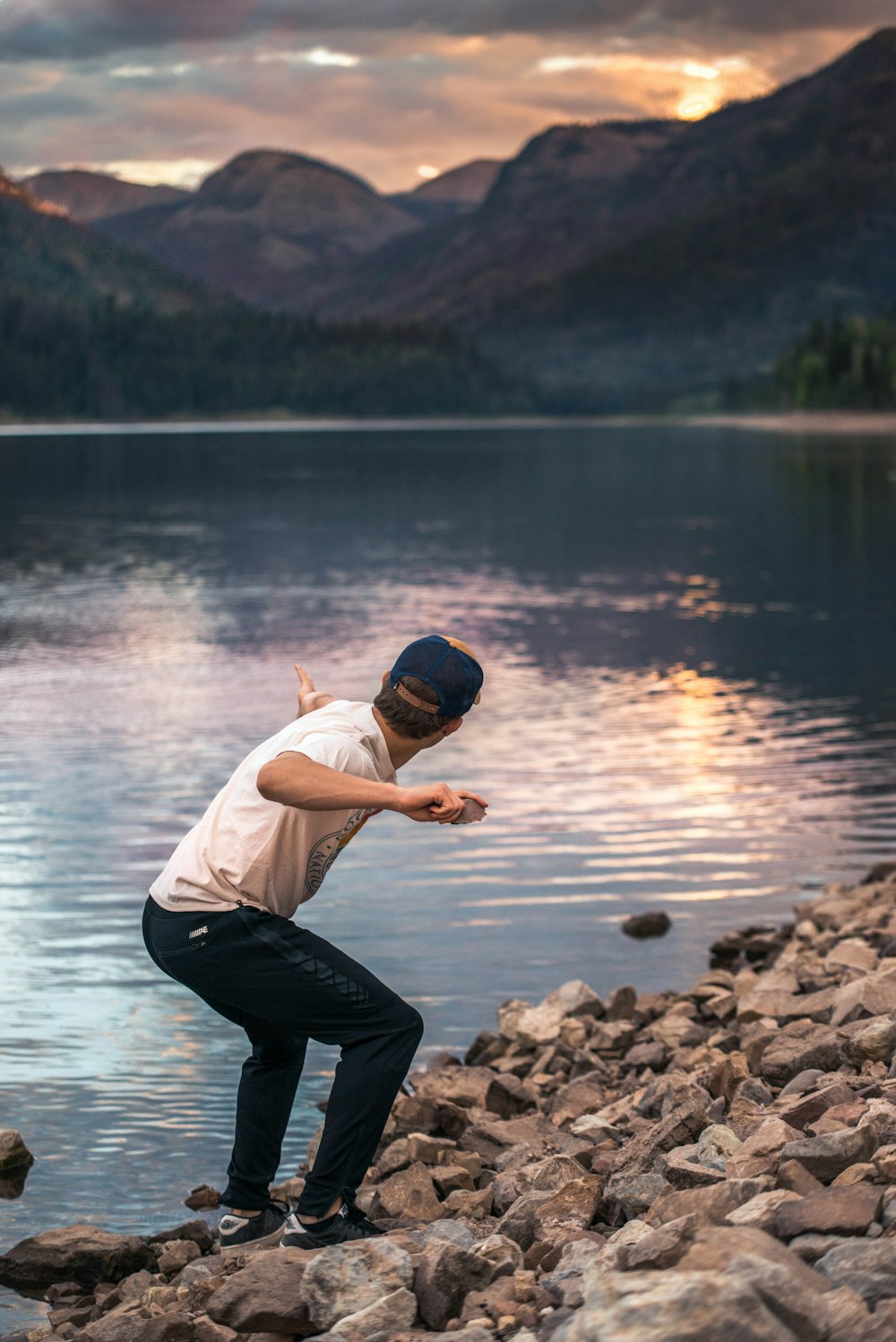 man holding stone near body of water during golden hour