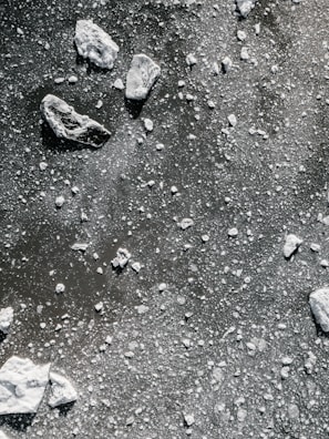 An overhead view of a frozen surface scattered with numerous small, white ice chunks and larger pieces of ice. The uneven distribution creates a textured and layered appearance, with the contrast between the white ice and the darker background enhancing the details.