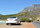 Elegant black Mercedes Classe V parked by a sunlit Sardinian coastline.