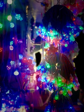 Colorful strings of LED lights hang closely together, casting vibrant hues of red, blue, green, and purple. The lights are intertwined and create a visually striking pattern against a dark background, with a festive and lively atmosphere.