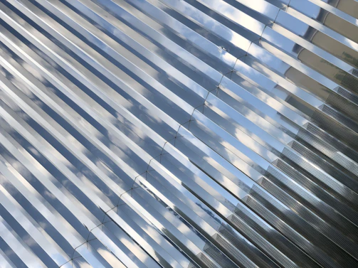 Detail of reflective glass panels catching the sky, integrated with aluminum framing.