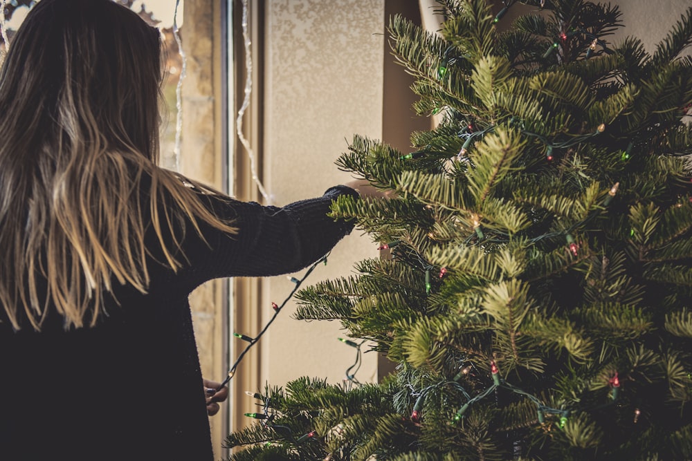 mujer instalando guirnaldas de luces en el árbol de Navidad