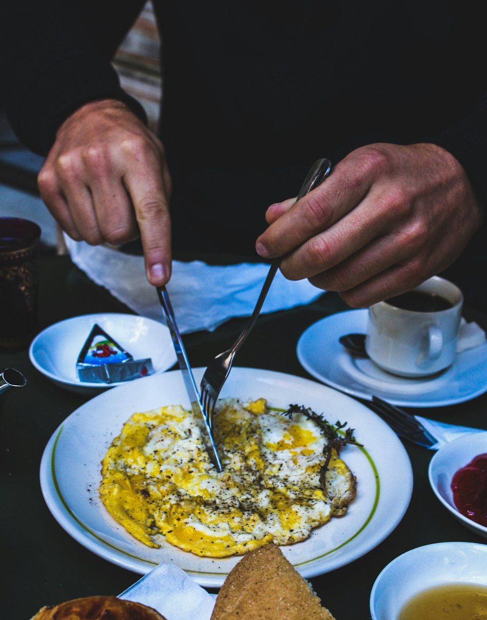 person holding butter knife and fork over cooked egg