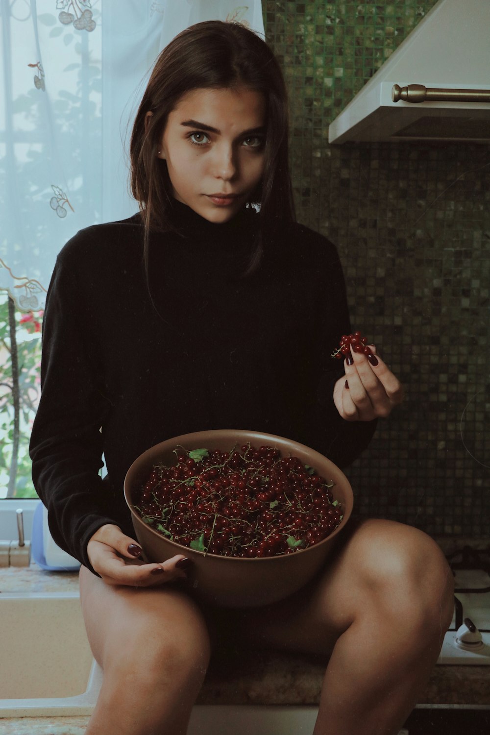 woman wearing long-sleeved shirt holding berries and container while sitting