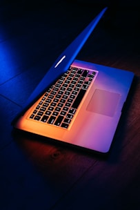 A modern refurbished notebook open on a desk with a cosmic blue and violet light reflecting off its surface.