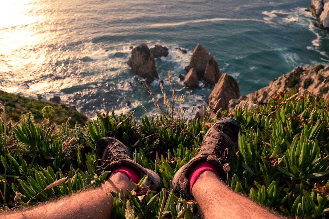 person sitting on cliff near sea during daytime