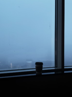 A quiet moment of reflection with a notebook and coffee beside a window overlooking a city skyline.
