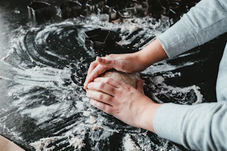 Hands kneading dough on a wooden board with flour scattered around.