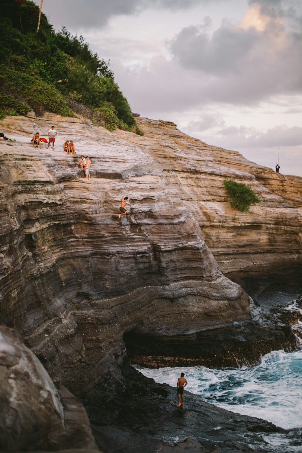 group of people sitting on rock in front of body of water