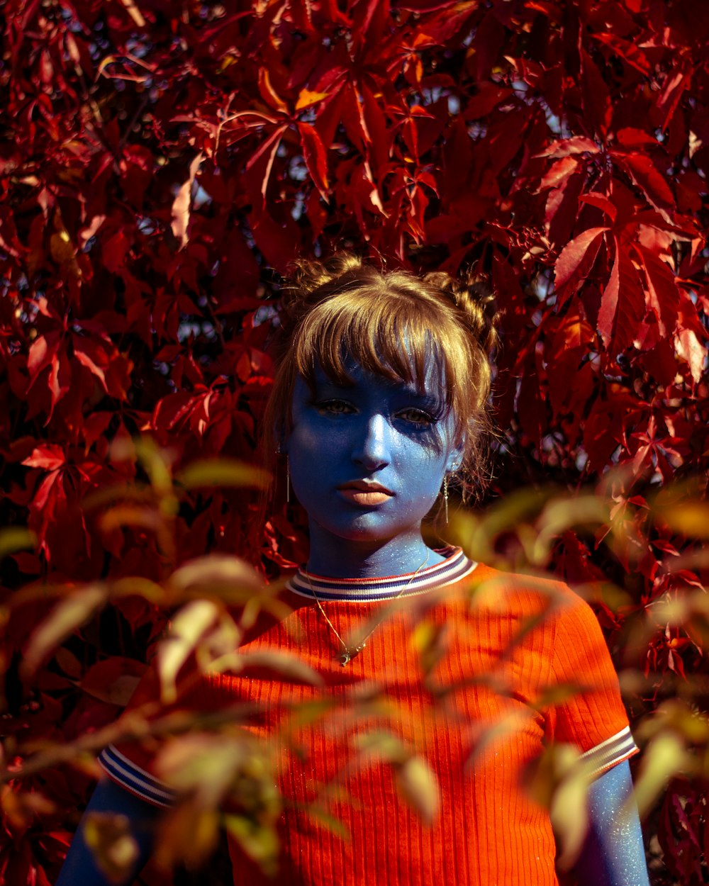 blue skinned girl wearing red crew-neck shirt surrounded by red maple leaves