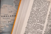An open dictionary page with text in a foreign language, possibly German, showing various terms and their definitions. Next to it, a blurred map partially visible with the word 'ENGLAND' and parts of the coastline.