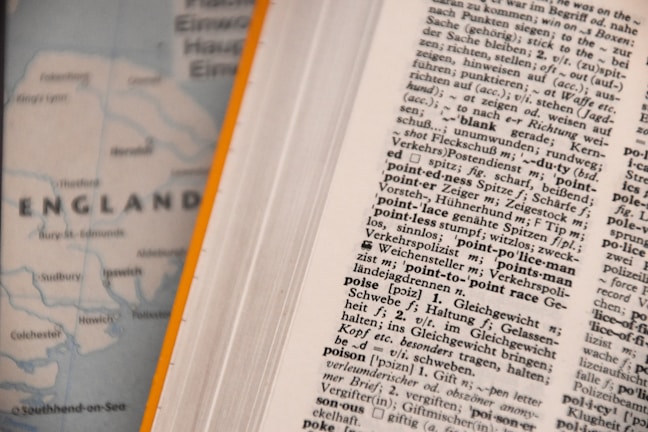 An open dictionary page with text in a foreign language, possibly German, showing various terms and their definitions. Next to it, a blurred map partially visible with the word 'ENGLAND' and parts of the coastline.