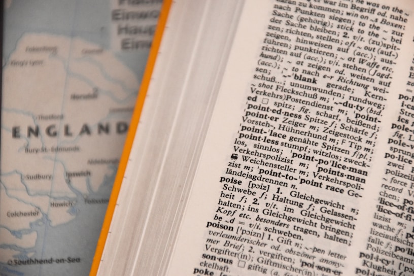 An open dictionary page with text in a foreign language, possibly German, showing various terms and their definitions. Next to it, a blurred map partially visible with the word 'ENGLAND' and parts of the coastline.