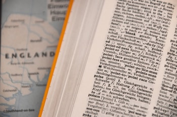 An open dictionary page with text in a foreign language, possibly German, showing various terms and their definitions. Next to it, a blurred map partially visible with the word 'ENGLAND' and parts of the coastline.