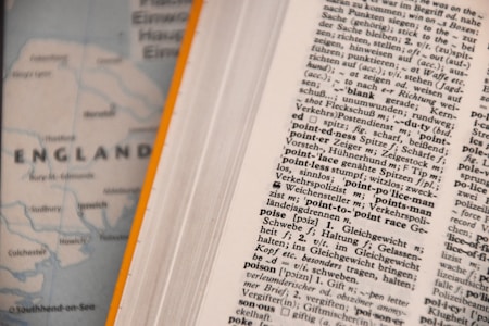An open dictionary page with text in a foreign language, possibly German, showing various terms and their definitions. Next to it, a blurred map partially visible with the word 'ENGLAND' and parts of the coastline.