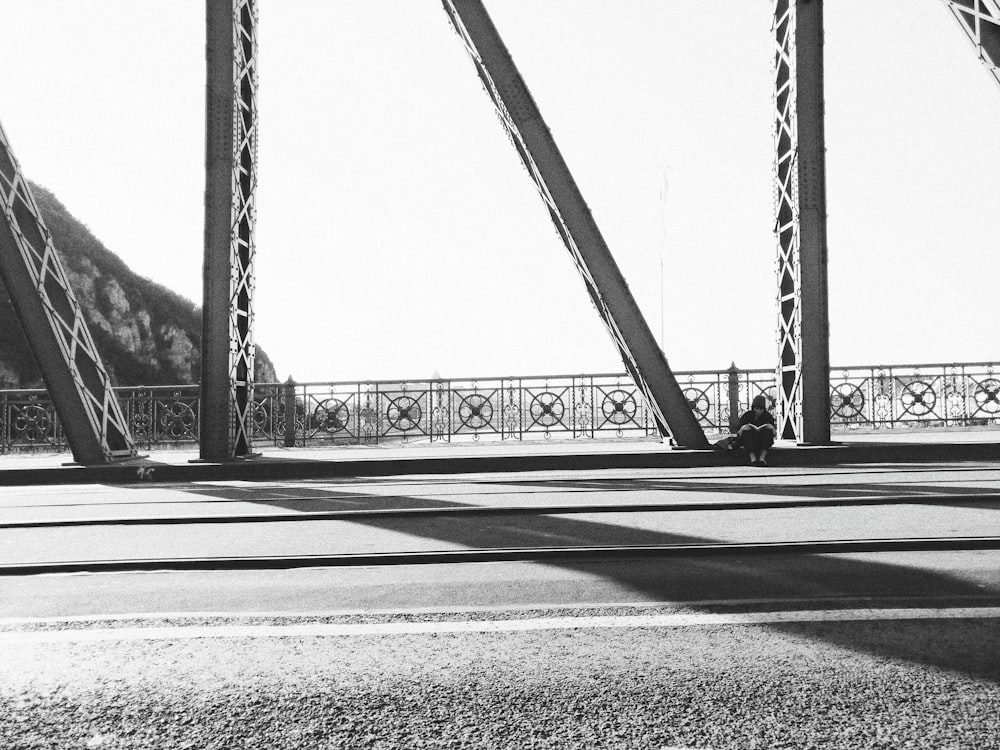 grayscale photography of person sitting on bridge