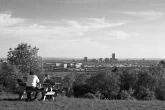 A couple enjoying a picnic on a grassy hill with their train visible in the distance.