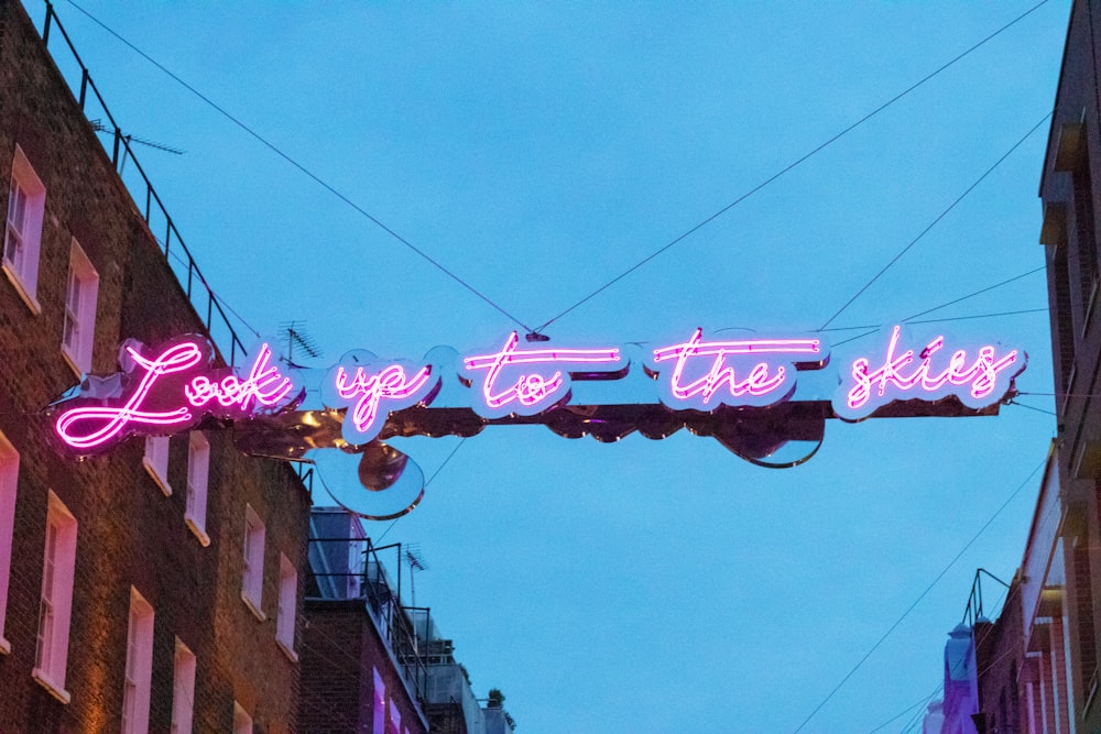 pink and blue Look Up To The Skies neon signage hanging in between buildings